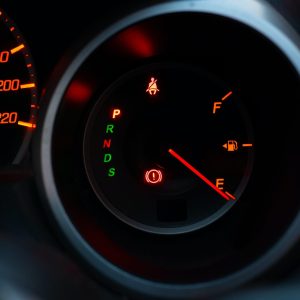 Close up of meter panel with the needle pointing at E on black blackground, car has run out of gas